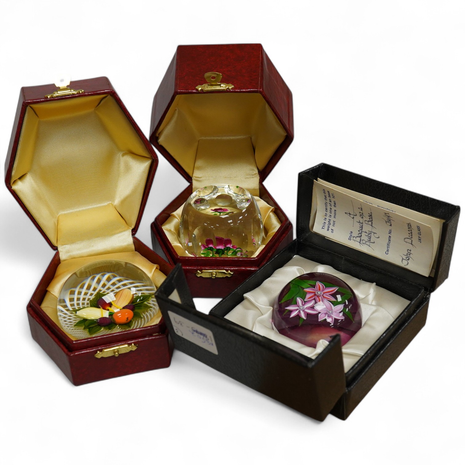Two Perthshire lamp work glass paperweights, fruit weight, 52/350, rose and bud weight, 69/300 together with a John Deacons bouquet on a ruby base paperweight, edition of 101 (3)